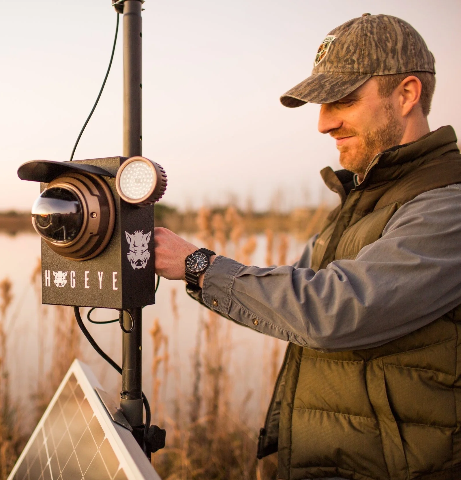 Man in cap and vest installing a HogEye camera on a trap